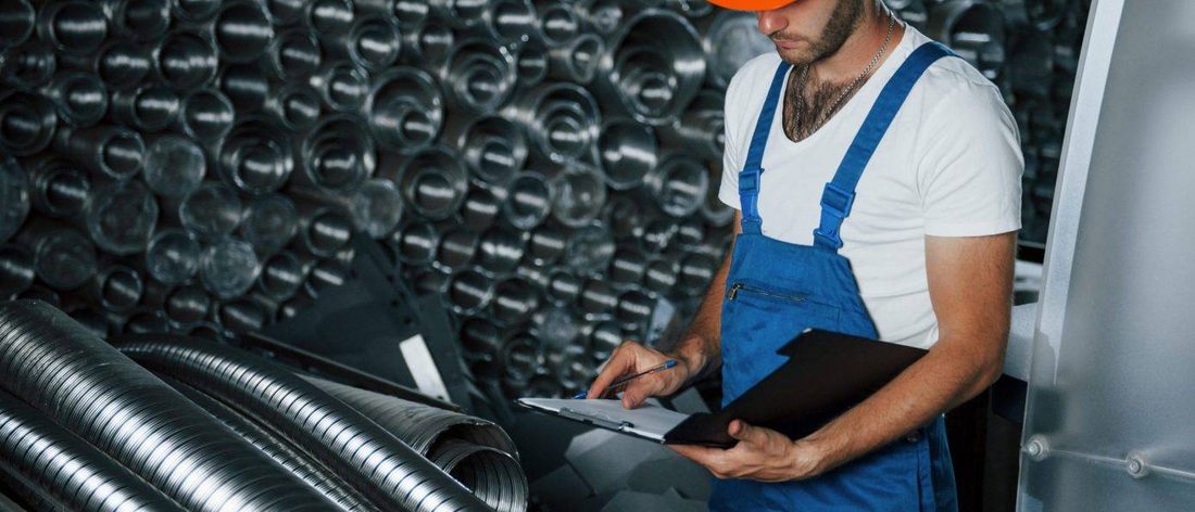 Técnico de mantenimiento con overol revisando ductos de ventilación con su tabla de registro
