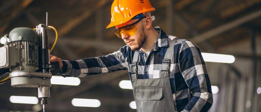 Técnico con casco naranja y lentes operando un taladro de columna en una planta industrial