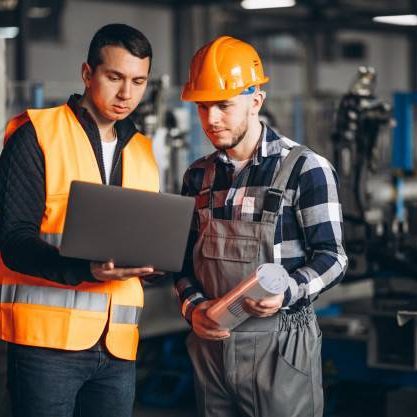 Dos técnicos con casco y chaleco revisando datos en la planta
