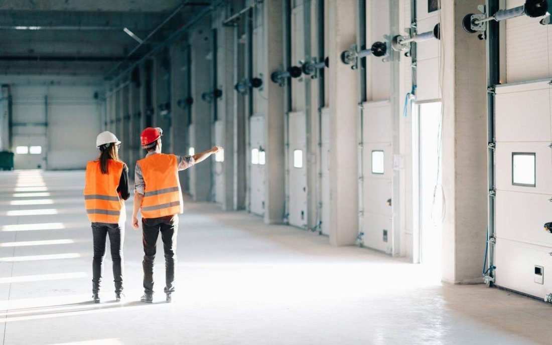 Dos técnicos con chaleco y casco recorriendo una nave industrial